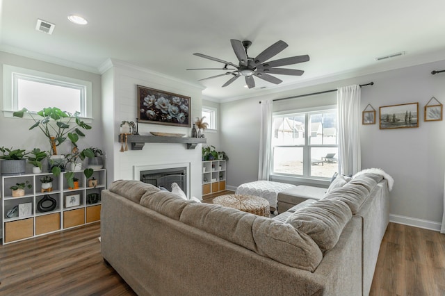 living area with visible vents, a glass covered fireplace, dark wood-type flooring, and ornamental molding