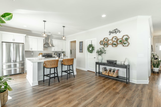 kitchen with a breakfast bar area, white cabinetry, appliances with stainless steel finishes, wall chimney exhaust hood, and a center island with sink