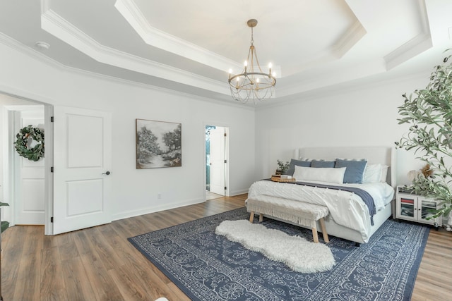 bedroom featuring baseboards, wood finished floors, a tray ceiling, crown molding, and a chandelier