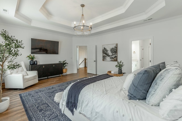 bedroom with a tray ceiling, visible vents, a notable chandelier, and wood finished floors