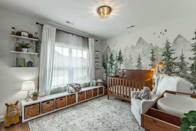 bedroom with a nursery area, visible vents, and wood finished floors