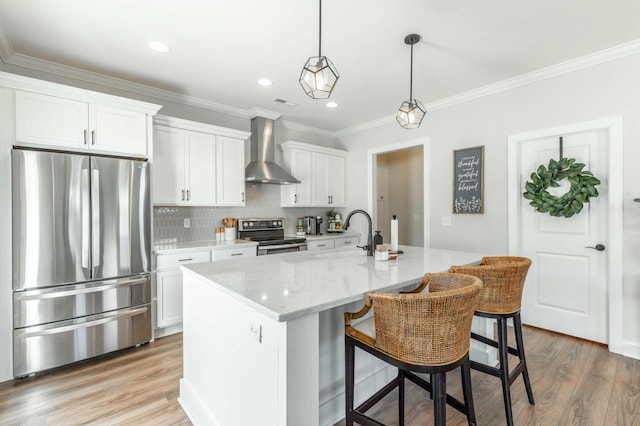 kitchen with an island with sink, wall chimney range hood, white cabinetry, and appliances with stainless steel finishes