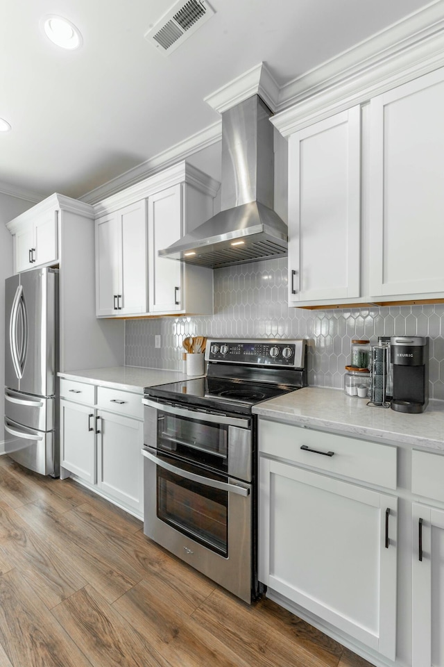 kitchen featuring stainless steel appliances, visible vents, white cabinetry, wood finished floors, and wall chimney exhaust hood