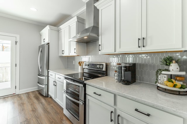 kitchen with white cabinets, light stone counters, stainless steel appliances, light wood-type flooring, and wall chimney range hood