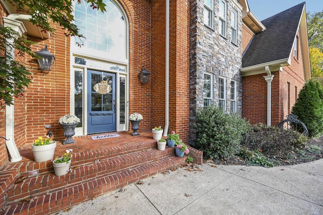 entrance to property featuring stone siding, brick siding, and a shingled roof