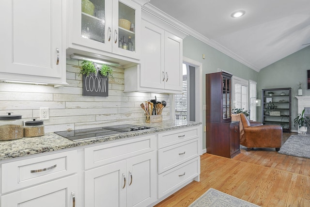 kitchen with light wood-style flooring, glass insert cabinets, black electric stovetop, vaulted ceiling, and white cabinetry