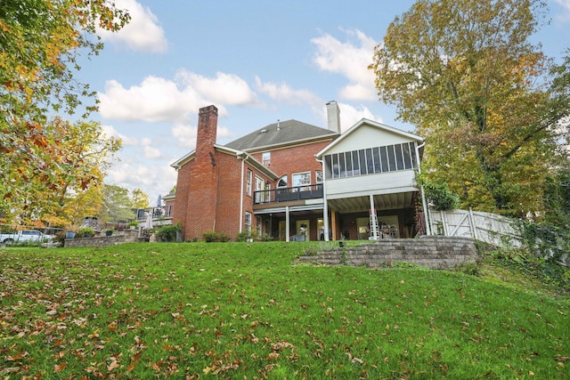 rear view of property with brick siding, a yard, a chimney, a sunroom, and fence