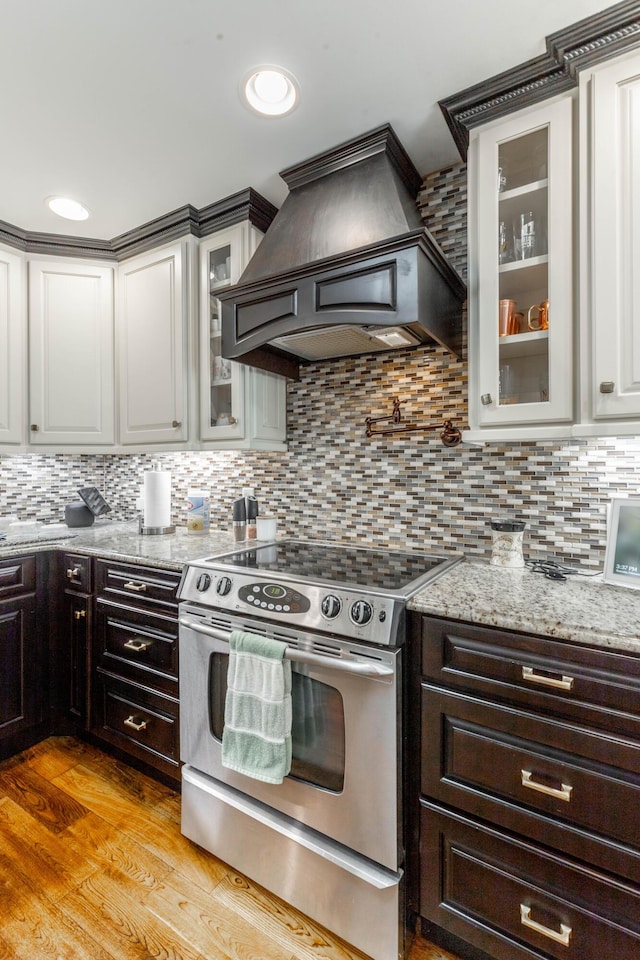 kitchen featuring tasteful backsplash, electric range, light wood-style flooring, light stone countertops, and custom exhaust hood