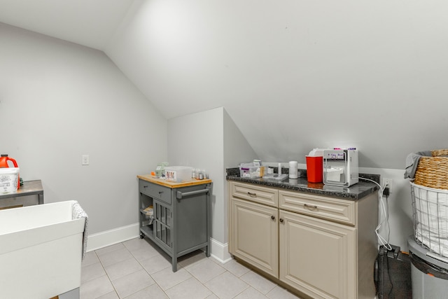 kitchen with cream cabinetry, light tile patterned floors, dark countertops, vaulted ceiling, and baseboards