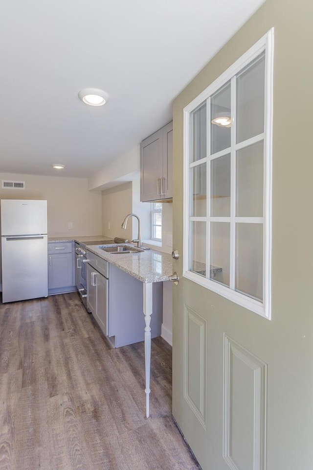 kitchen featuring visible vents, gray cabinetry, freestanding refrigerator, a sink, and a peninsula