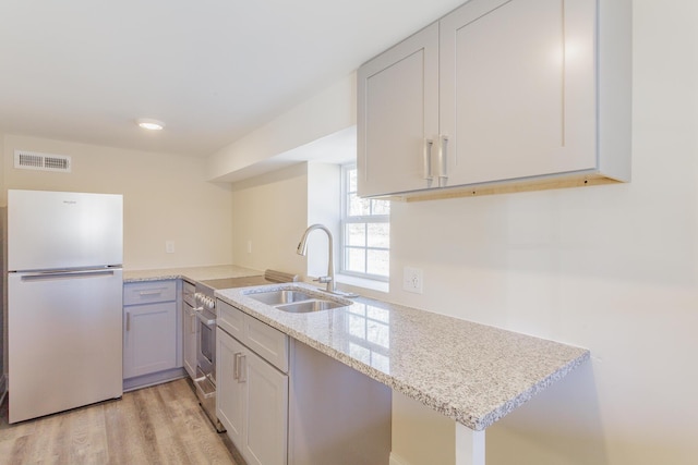 kitchen with light stone counters, visible vents, light wood-style flooring, freestanding refrigerator, and a sink