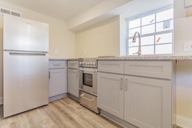 kitchen with light wood-style flooring, stainless steel stove, gray cabinetry, visible vents, and freestanding refrigerator