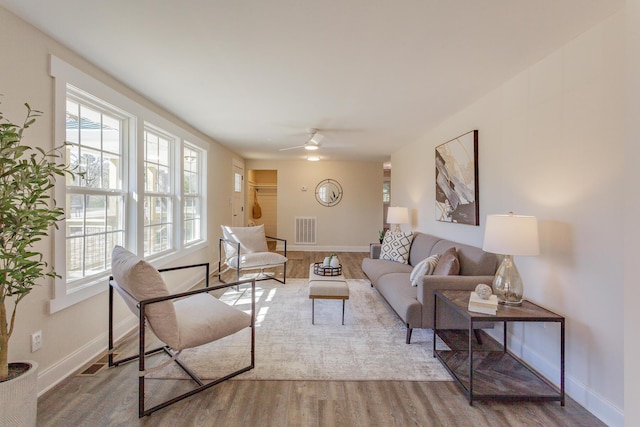 living room featuring a ceiling fan, baseboards, visible vents, and wood finished floors