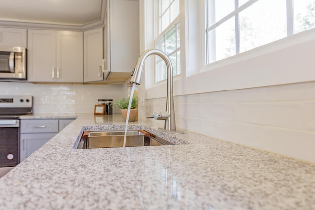 kitchen featuring a sink, appliances with stainless steel finishes, gray cabinets, light stone countertops, and tasteful backsplash