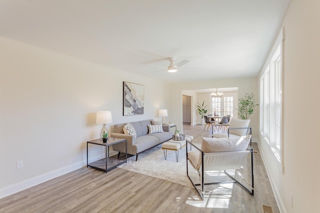 living area with baseboards, light wood finished floors, and ceiling fan with notable chandelier