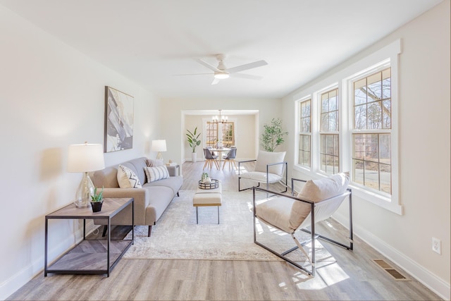 living room with ceiling fan with notable chandelier, wood finished floors, visible vents, and baseboards