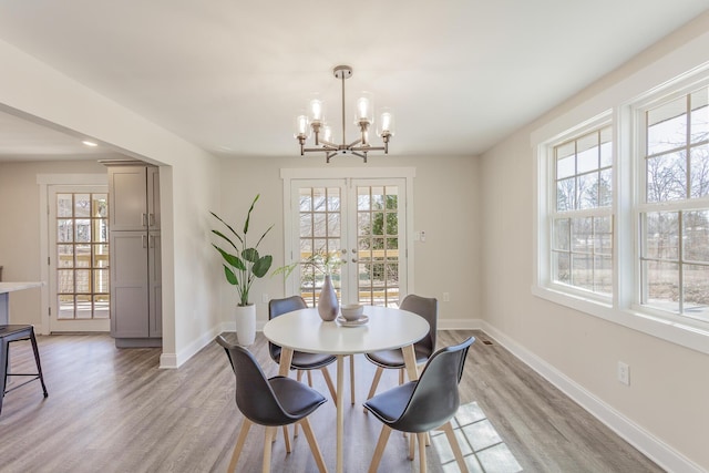 dining area featuring light wood finished floors, french doors, a chandelier, and baseboards