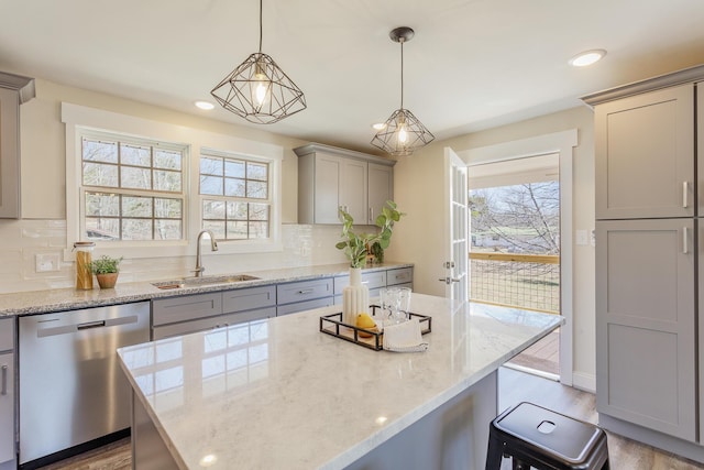 kitchen with light stone counters, tasteful backsplash, gray cabinets, stainless steel dishwasher, and a sink