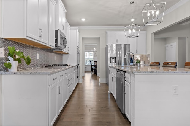 kitchen featuring a center island with sink, decorative light fixtures, appliances with stainless steel finishes, white cabinets, and ornamental molding