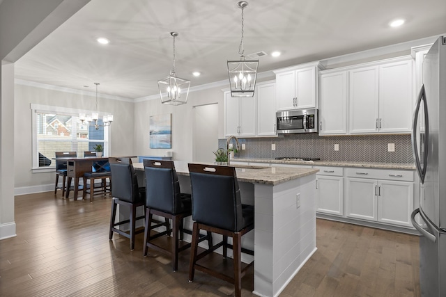 kitchen with stainless steel appliances, white cabinets, decorative light fixtures, light stone counters, and a center island with sink