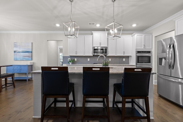 kitchen with a kitchen island with sink, hanging light fixtures, stainless steel appliances, and light stone countertops