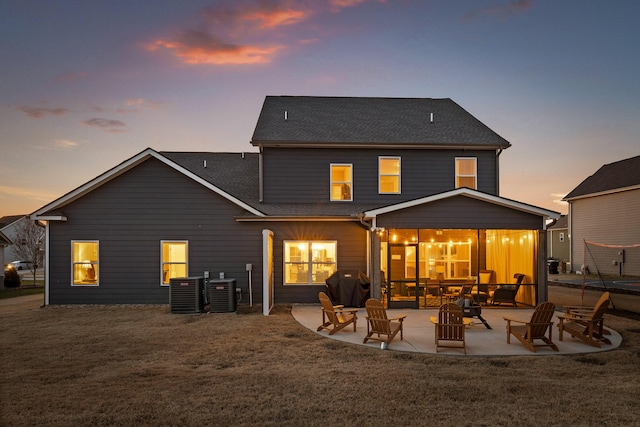 back house at dusk with cooling unit, a patio area, and a lawn