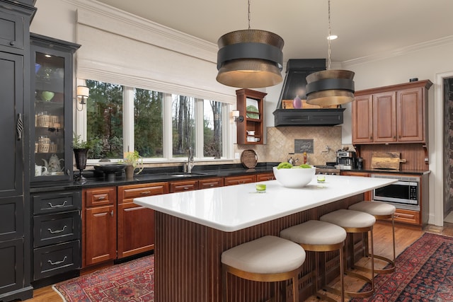 kitchen with a center island, brown cabinets, crown molding, stainless steel microwave, and glass insert cabinets