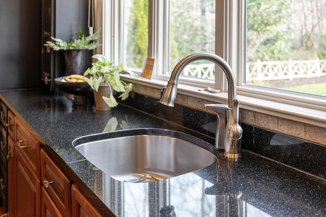 room details featuring brown cabinetry, dark stone countertops, and a sink