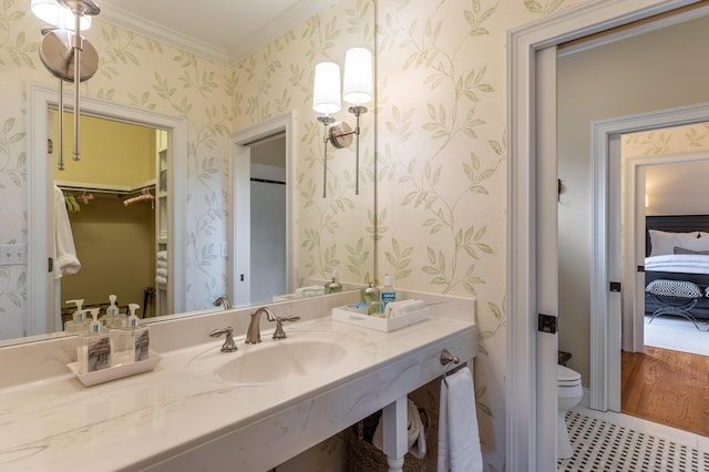 bathroom featuring wallpapered walls, toilet, ornamental molding, a walk in closet, and a sink