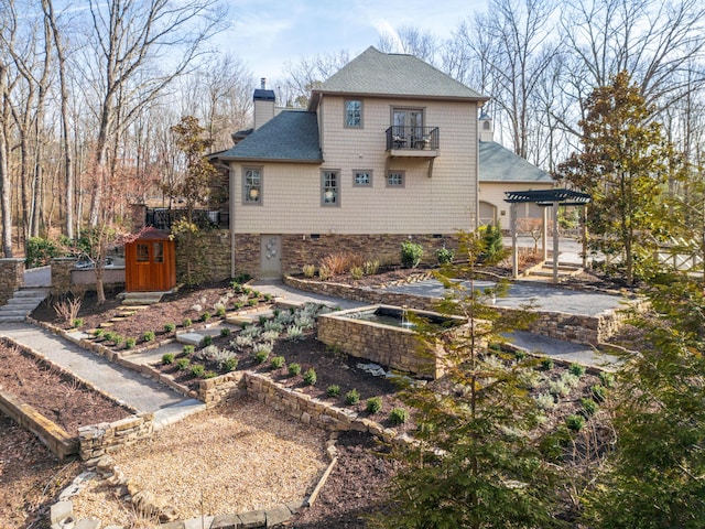 rear view of property featuring an outbuilding, a balcony, a storage shed, a shingled roof, and a chimney