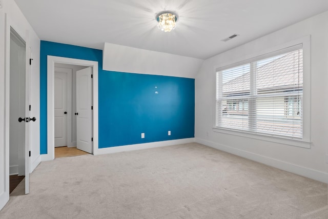 unfurnished room featuring baseboards, visible vents, vaulted ceiling, and light colored carpet