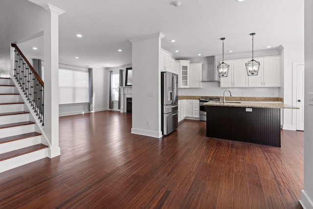 kitchen featuring a kitchen island with sink, stainless steel appliances, wall chimney range hood, light stone countertops, and glass insert cabinets