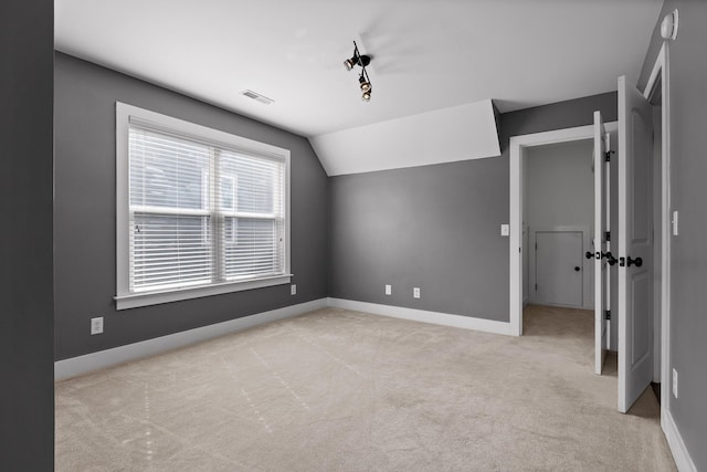 interior space featuring lofted ceiling, light colored carpet, visible vents, and baseboards