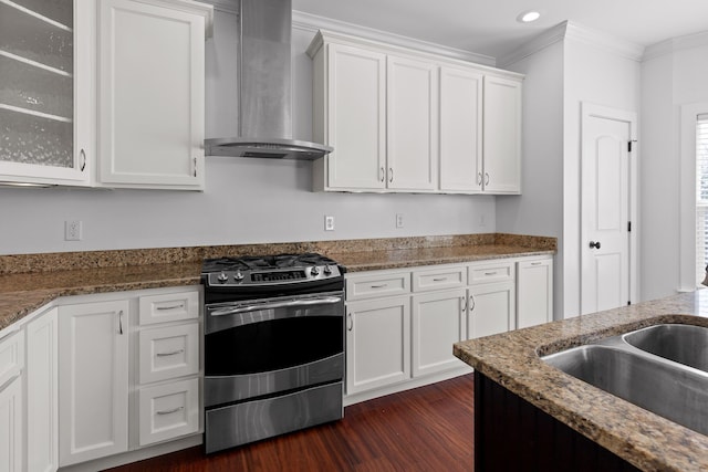 kitchen with dark stone counters, gas range, wall chimney exhaust hood, glass insert cabinets, and white cabinetry