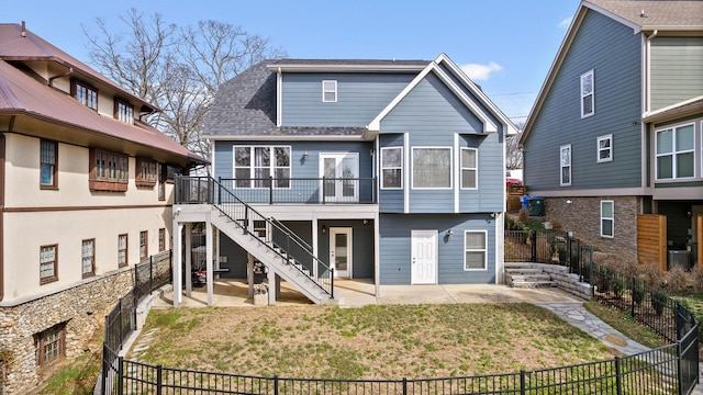 rear view of house featuring a patio, a fenced backyard, a shingled roof, stairs, and a yard