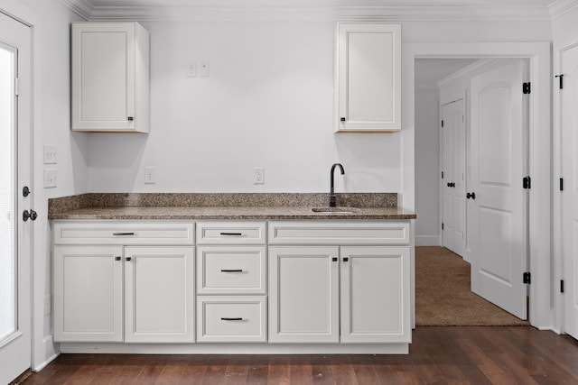 kitchen with dark wood finished floors, ornamental molding, white cabinets, a sink, and dark stone counters