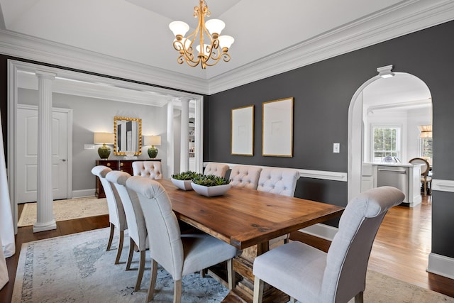 dining room with arched walkways, crown molding, wood finished floors, and decorative columns