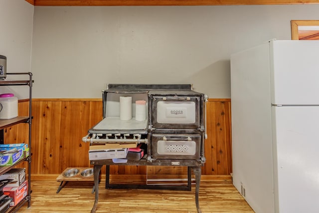 details with light wood-style floors, freestanding refrigerator, wainscoting, and wooden walls