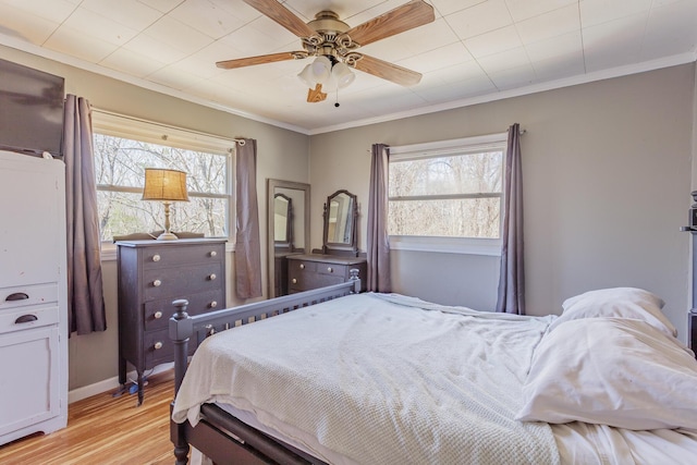 bedroom with ornamental molding, light wood-type flooring, a ceiling fan, and baseboards