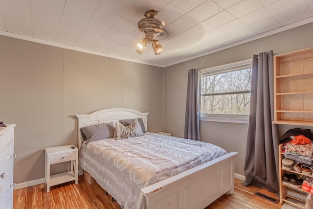 bedroom with baseboards, light wood-style flooring, visible vents, and crown molding