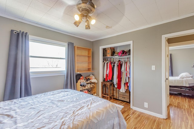 bedroom featuring a closet, light wood-style floors, ornamental molding, ceiling fan, and baseboards