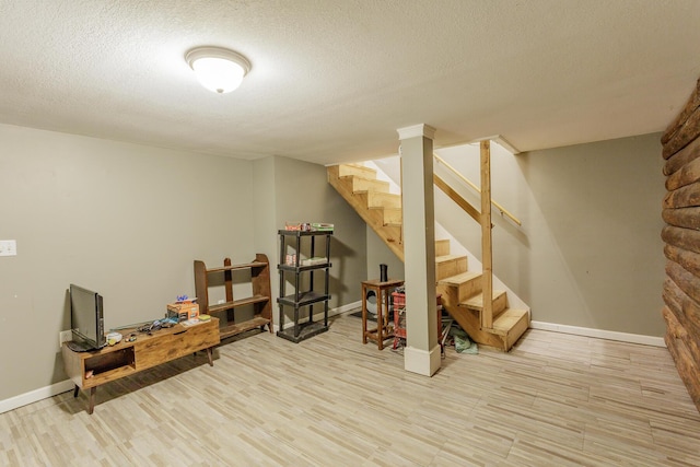 finished basement featuring light wood-style floors, stairs, baseboards, and a textured ceiling