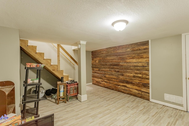 finished basement featuring visible vents, stairway, a textured ceiling, light wood-type flooring, and wood walls