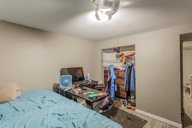 bedroom featuring light wood-style flooring, a textured ceiling, baseboards, and a closet