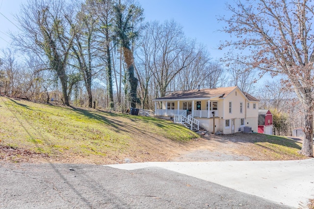 view of front facade with dirt driveway, a porch, cooling unit, and a front yard