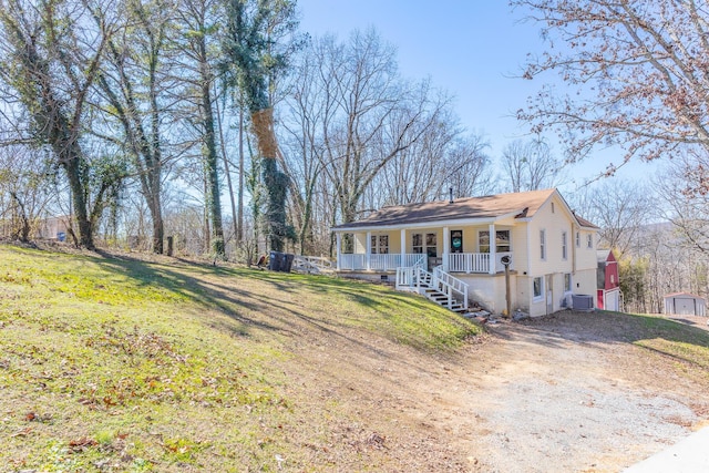 view of front of property featuring dirt driveway, a porch, central AC, and a front yard