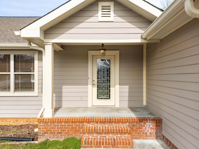 entrance to property featuring covered porch and roof with shingles