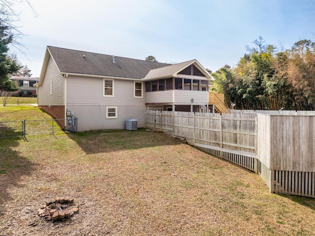 back of property featuring cooling unit, a fenced backyard, a sunroom, stairway, and a lawn