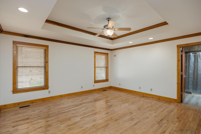 empty room with baseboards, visible vents, light wood-style flooring, a tray ceiling, and crown molding