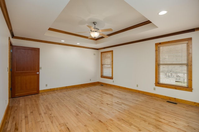 unfurnished room featuring light wood finished floors, visible vents, baseboards, a tray ceiling, and crown molding